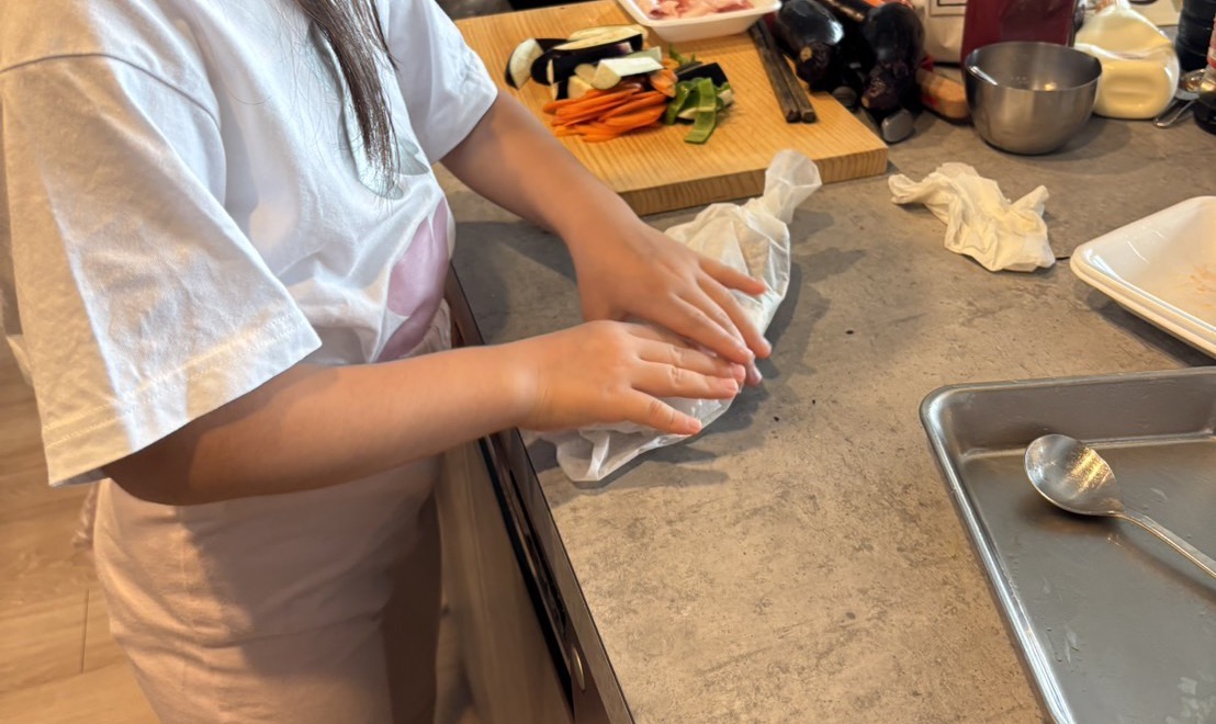子どもの手で、鮭と野菜をクッキングシートで包んでいるところ